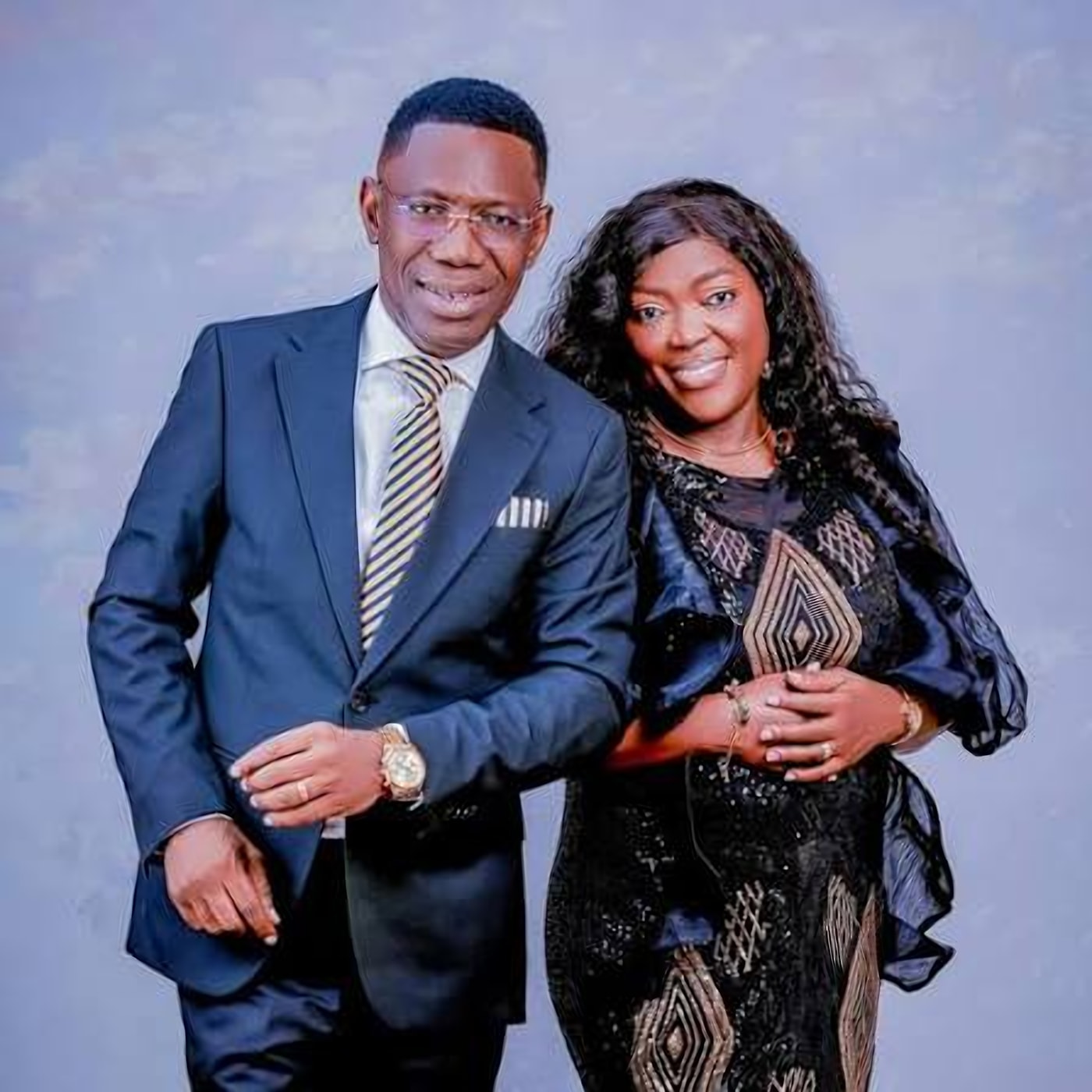 Rev. Dr. Sam Oye in a navy suit and striped tie with his wife, Pastor Mary Sam Oye, in a black embellished dress, smiling arm in arm